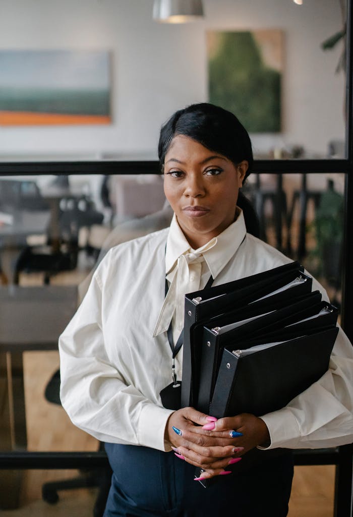 Professional businesswoman confidently holding office binders in a modern workspace.