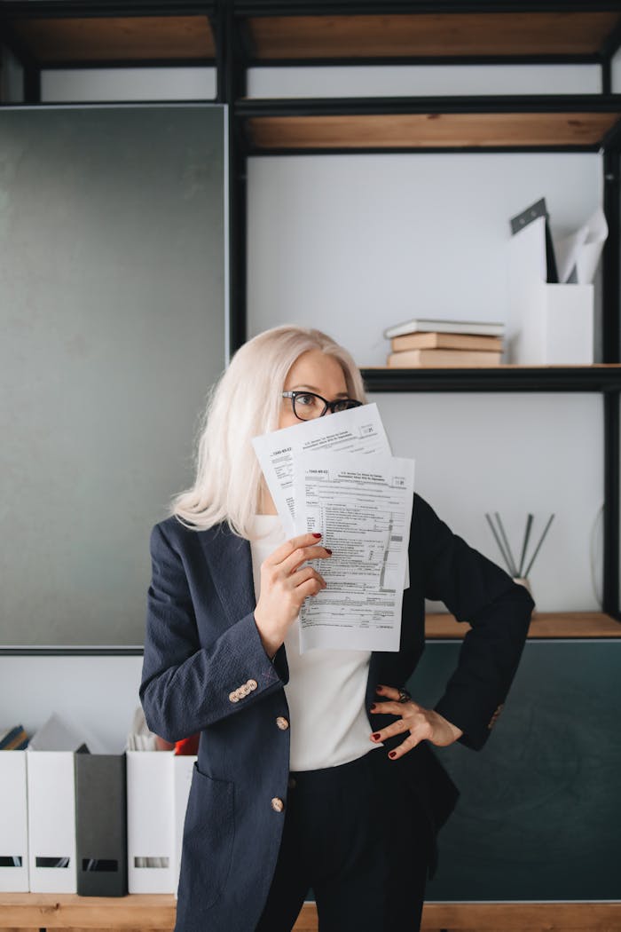Businesswoman with glasses holding papers in a modern office setting.